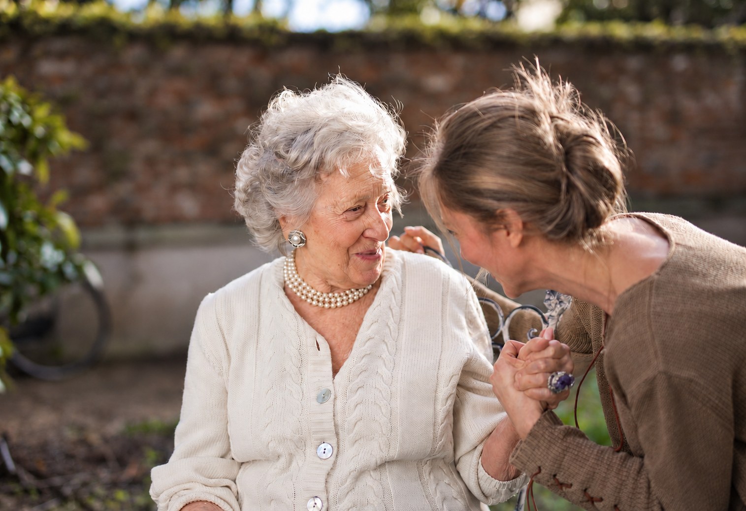 Seniorin sitzt im Garten und wird von einer Betreuungskraft an der Hand gehalten