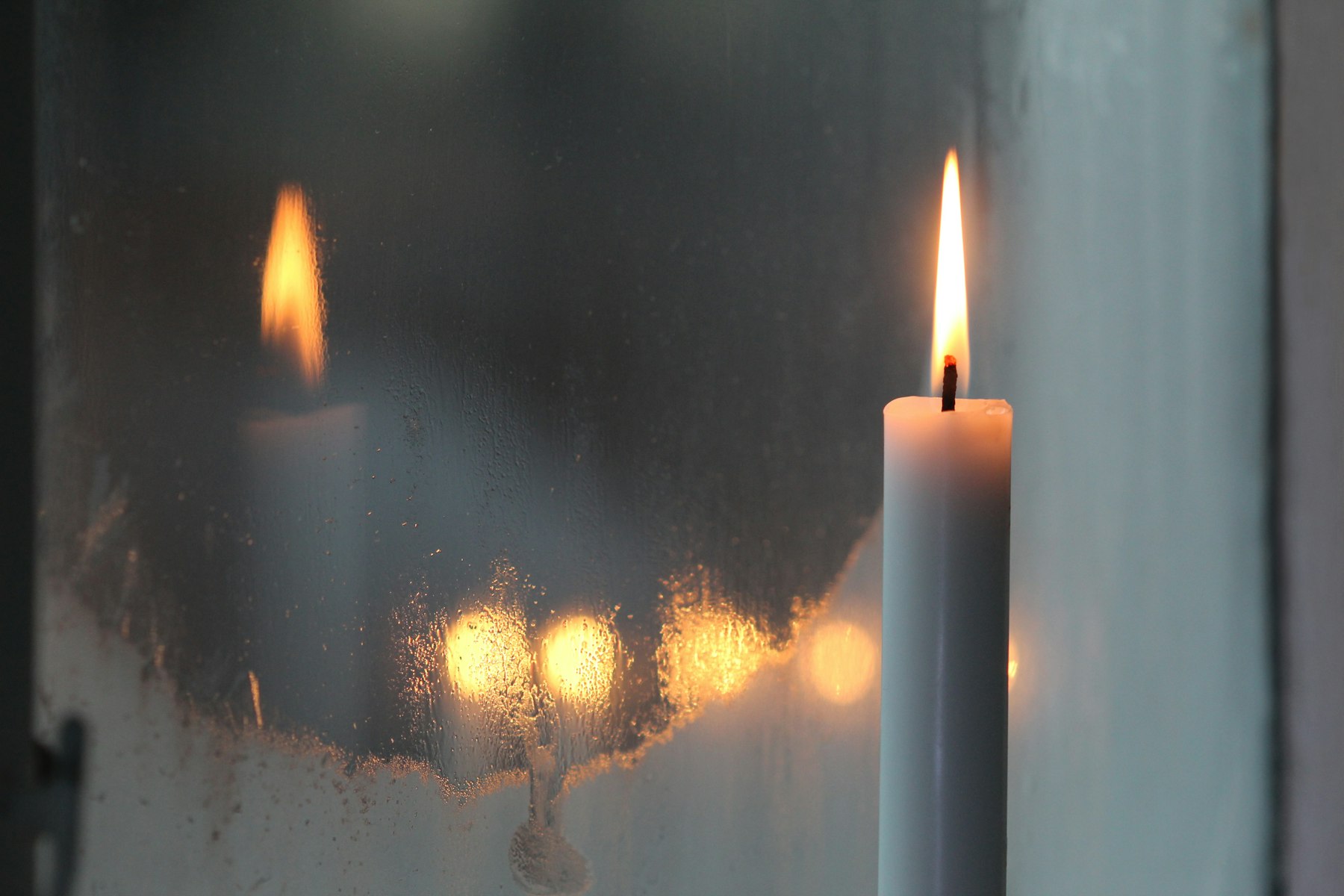 Brennende Kerze am Fenster mit warmen Lichtern im Hintergrund